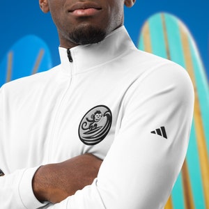 May include: White zippered jacket with a black embroidered logo of a monkey surfing on a wave. The logo is on the left side of the chest. The jacket has a black Adidas logo on the right sleeve.