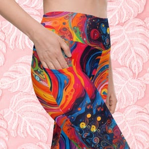May include: Colorful leggings with a high waist and a pocket on the left side. The leggings feature a swirling abstract pattern in shades of red, orange, yellow, blue, and black.