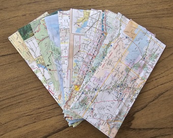 May include: A collection of folded paper maps, some with text like "Buffalo" and "Regina" visible. The maps are arranged in a fan shape on a wooden surface.