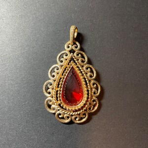 May include: A gold pendant with a red teardrop-shaped gemstone set in a filigree design.
