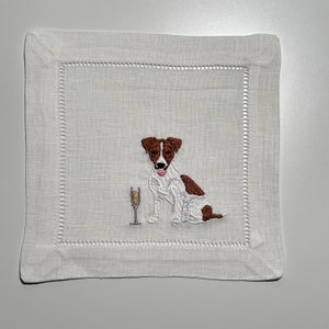 Puede incluir: Servilleta de cóctel de lino blanco con una imagen bordada de un perro marrón y blanco con una copa de champán.
