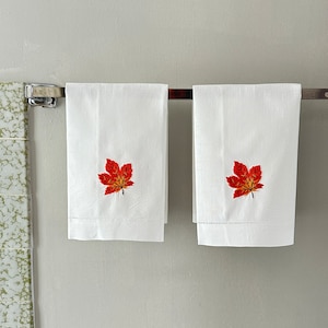 May include: Two white hand towels with embroidered red and orange maple leaves.