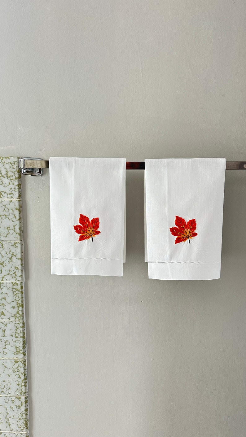 May include: Two white hand towels with embroidered red and orange maple leaves.