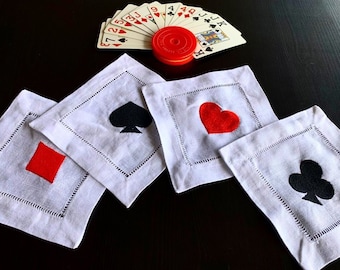 Peut inclure: Quatre serviettes en lin blanc avec des motifs de cartes à jouer brodés : un carreau rouge, un cœur rouge, une pique noire et un trèfle noir.