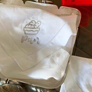 May include: White linen napkin with embroidered bread basket and the word "Pain" in cursive.