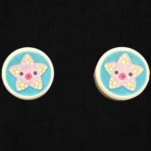 May include: Two small, round, white buttons with a blue background and a pink starfish with yellow dots on each.