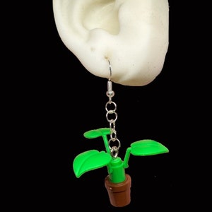 May include: Green plant earrings with a brown pot and silver chain. The plant has two green leaves on each side.
