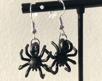 May include: A pair of black spider earrings with silver hooks. The spiders have eight legs and a detailed body.
