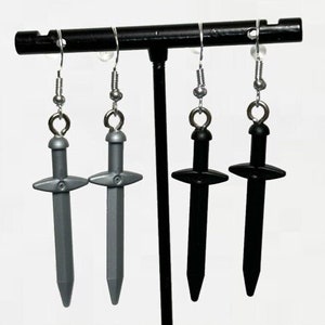 Pode incluir: Um par de brincos com pingentes em forma de espada. Um par é prateado e o outro é preto.