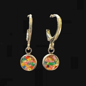 May include: A pair of silver-toned hoop earrings. Each earring features a small, round pendant filled with colorful, crushed stone fragments. The stones include shades of red, yellow, blue, and green. The earrings hang against a black background.