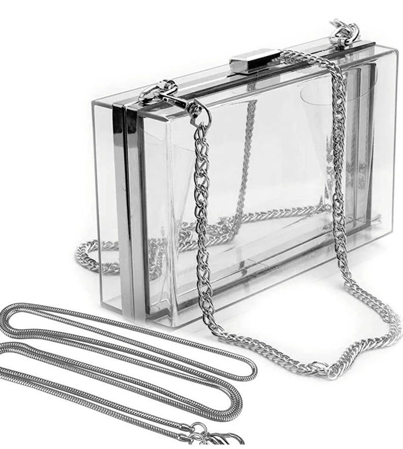 May include: A clear plastic clutch bag with a silver chain strap. The bag has a silver clasp and a second, thinner silver chain strap.