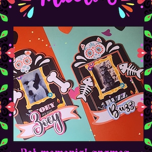 May include: Pet memorial frames with Day of the Dead theme. The frames feature photos of pets, with decorative elements like bones, fish skeletons, and sugar skull designs. The frames have the names "Zoey" and "Buzz" on them.