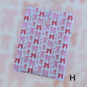 May include: White laptop sleeve with a pink and red bow pattern. The sleeve has a button closure and the letter "H" is visible in the bottom right corner.