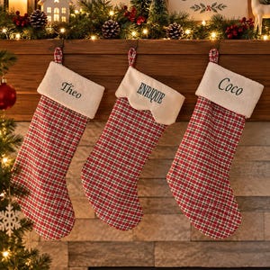 Peut inclure: Trois chaussettes de Noël avec un motif à carreaux rouge, blanc et vert. Les chaussettes gauche et droite ont des revers en sherpa blanc brodés avec les prénoms Theo et Coco. La chaussette centrale a un revers crème festonné avec le nom ENRIQUE.