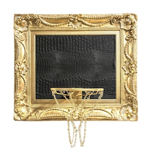 Peut inclure: Une image encadrée en or avec un fond noir en cuir de crocodile et un panier de basket en or avec un filet en chaîne suspendu.