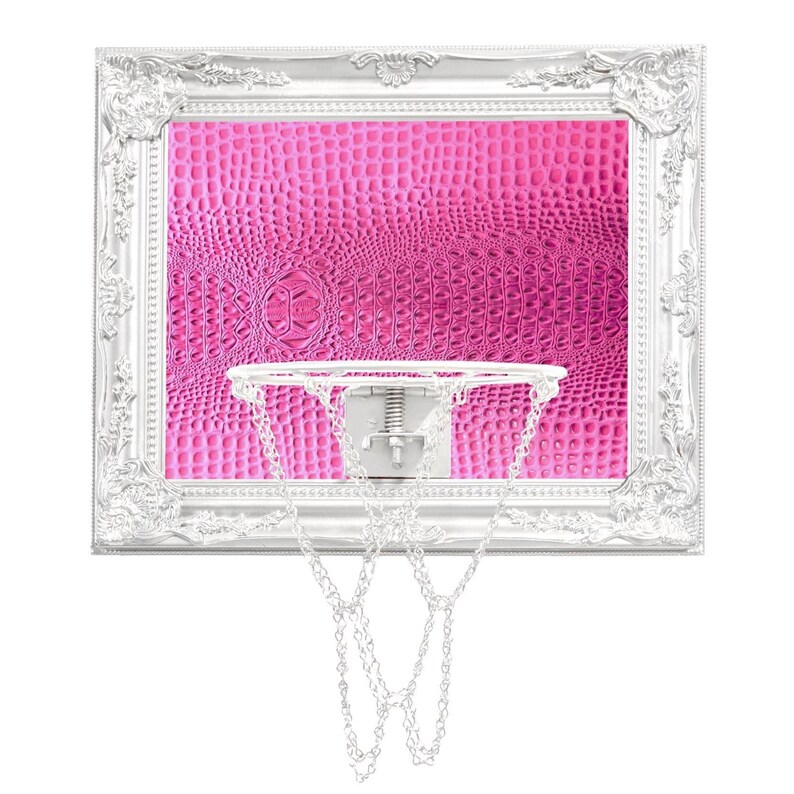 May include: A white basketball hoop with a pink crocodile patterned backboard in a silver ornate frame. The hoop has a white metal rim and a chain net.