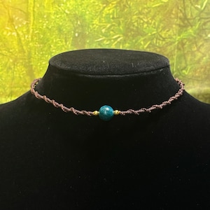 May include: A brown cord choker necklace with a single teal blue gemstone bead.