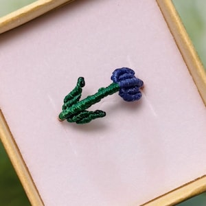 May include: A blue and green flower ring made of fabric. The flower is a single bloom with a green stem and leaves.