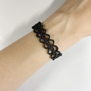 May include: A black choker necklace with a delicate, intricate design. The necklace is made of a thin, flexible material and has a simple, elegant look.
