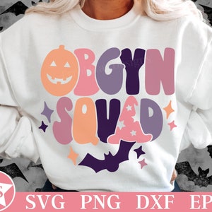 May include: A white crewneck sweatshirt featuring a colorful graphic with the text OBGYN SQUAD. The design includes a peach pumpkin, a purple witch hat, a dark purple bat, and small stars in shades of pink, orange, and purple on the front.