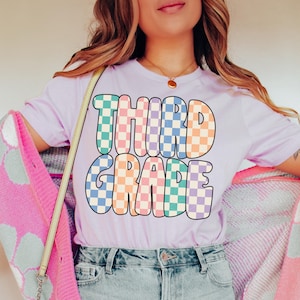 May include: A purple t-shirt with the words "THIRD GRADE" in a colorful checkered pattern.