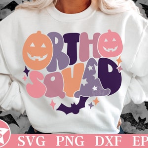 Könnte beinhalten: Ein weißes Sweatshirt mit Rundhalsausschnitt und einem farbenfrohen Grafikdruck mit dem Text "ORTHO SQUAD" in wellenförmiger Schrift. Das Design zeigt orangefarbene und rosafarbene Kürbisse, einen violetten Hexenhut mit Sternen und eine Fledermaus.