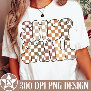 May include: White t-shirt with the text "SHOP SMALL" in brown and tan checkered letters.
