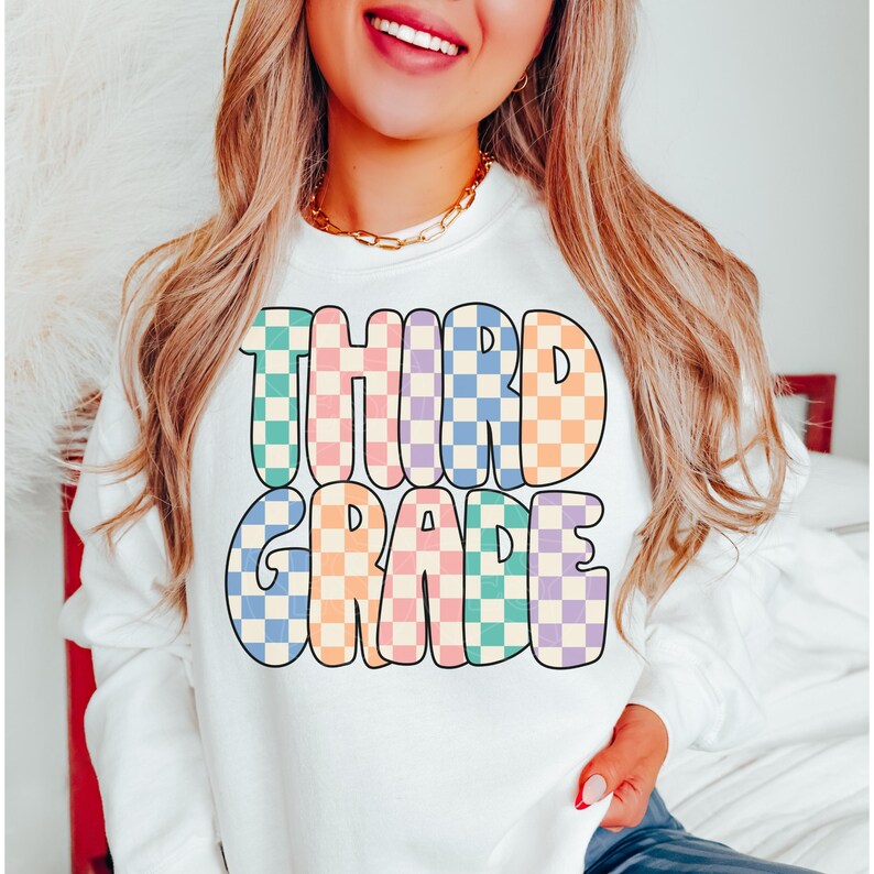May include: White sweatshirt with the text "THIRD GRADE" in colorful checkered letters.