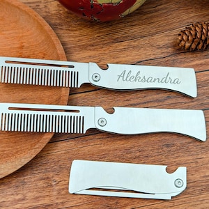Puede incluir: Tres peines plegables plateados, cada uno con un peine y un mango. Uno está grabado con el nombre "Aleksandra". Los peines están sobre una superficie de madera con un plato de madera, una piña y un globo decorativo.