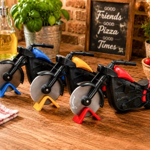Könnte beinhalten: Drei motorradförmige Pizzaschneider mit schwarzen Rahmen und kreisförmigen Edelstahlklingen. Die Motorräder haben blaue, gelbe und rote Kraftstofftanks, die jeweils auf einem passenden Ständer ruhen. Die Vorderräder dienen als Schneidklingen.