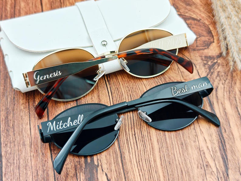 May include: Two pairs of sunglasses with personalized text. One pair has a gold frame with brown lenses and tortoise-shell arms, the other is black with dark lenses. The text on the frames reads "Genesis" and "Best man" and "Mitchell".