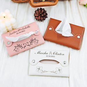 May include: Three leather tissue box holders in pink, brown, and white. The pink holder has a floral design and the text "Jaeden & Sabelle 22.10.2021". The white holder has a floral design and the text "Marsha & Clinton 22.10.2021".