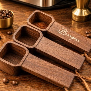 May include: Three dark brown wooden coffee scoops with square-shaped bowls and long handles. One handle features the engraved text Burgess. Each scoop includes a thin leather cord attached to the end of the handle for hanging purposes.