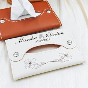 May include: Two tissue box holders. One is white with floral design and the names "Marsha & Clinton" and the date "22.10.2021". The other is brown. Both have silver snap closures and a curved opening for tissue access.