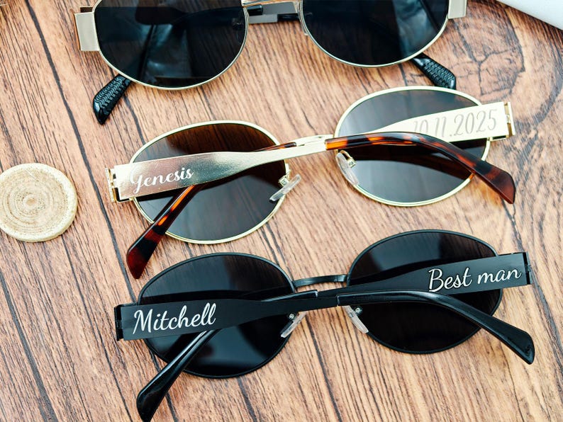 May include: Three pairs of sunglasses with dark lenses and personalized text on the frames. One pair is gold-toned, one has a tortoiseshell pattern, and the third is black. The text includes names and a date.