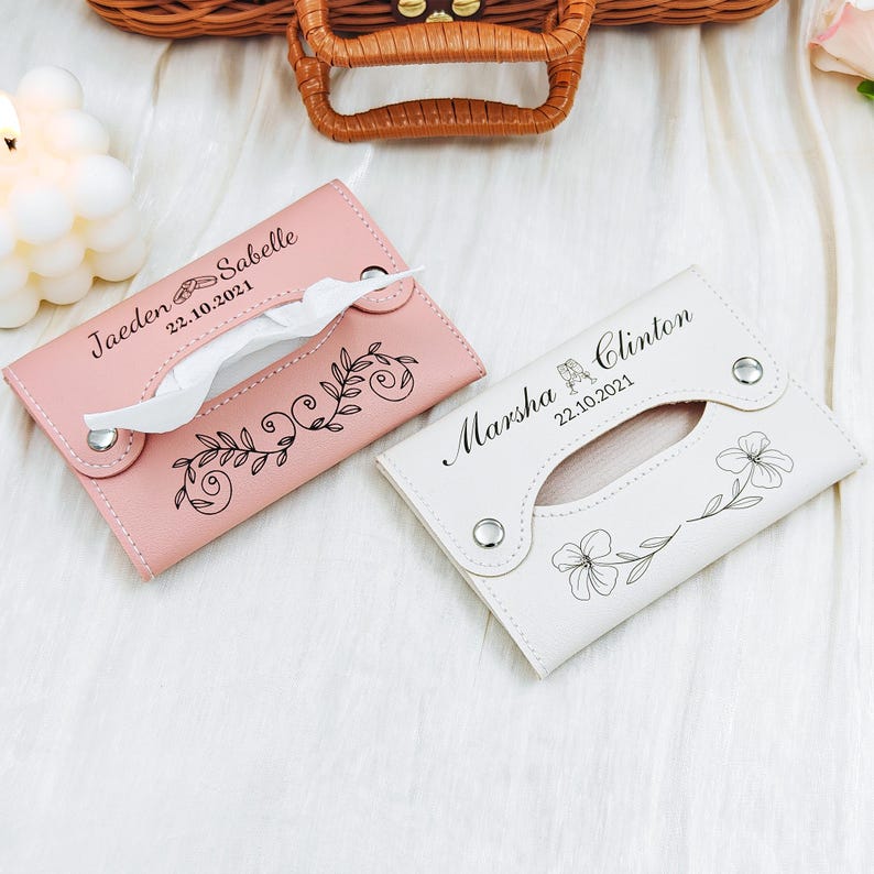 May include: Two personalized tissue holders. One is light pink with the name "Jaeden Sabelle" and the date "22.10.2021" and a floral design. The other is white with the name "Marsha Clinton" and the date "22.10.2021" and a floral design.