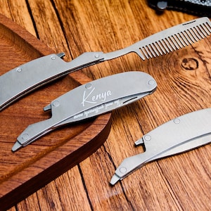 Könnte beinhalten: Ein Set aus Edelstahl-Pflegeutensilien, darunter ein Kamm und zwei Klapprasierer. Ein Rasierer ist mit dem Namen "Kenya" graviert. Die Werkzeuge werden auf einem Holztablett und einer Holzoberfläche präsentiert.
