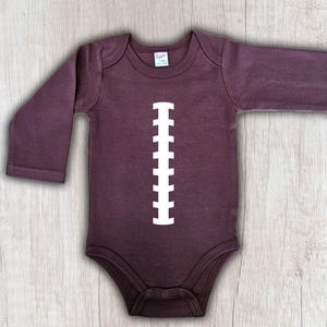 Peut inclure: Body b&eacute;b&eacute; violet fonc&eacute; &agrave; manches longues avec un motif de ballon de football blanc imprim&eacute; sur le devant. Le body a un col rond et des boutons-pression en bas. Le v&ecirc;tement est en mati&egrave;re douce.