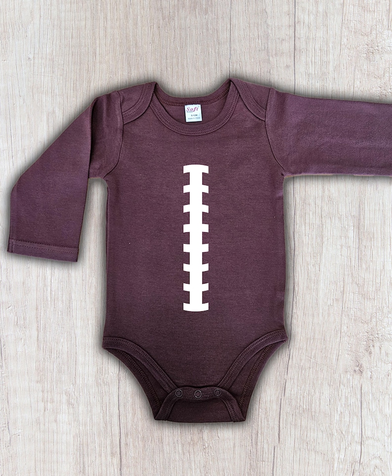Peut inclure: Body b&eacute;b&eacute; violet fonc&eacute; &agrave; manches longues avec un motif de ballon de football blanc imprim&eacute; sur le devant. Le body a un col rond et des boutons-pression en bas. Le v&ecirc;tement est en mati&egrave;re douce.