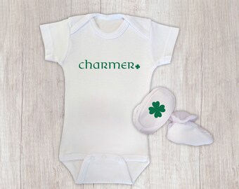 May include: White baby onesie with green text that says "charmer" and a green shamrock. The onesie is paired with white baby booties with a green shamrock on one.