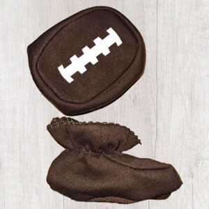 Peut inclure: Bottes de b&eacute;b&eacute; marron et un coussin assorti en forme de ballon de football. Le coussin a un motif cousu blanc. Les chaussons sont faits d'une mati&egrave;re douce et sont con&ccedil;us pour ressembler &agrave; un ballon de football.