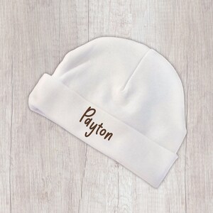 Peut inclure: Un bonnet de b&eacute;b&eacute; blanc avec un revers. Le nom "Payton" est brod&eacute; en marron sur le revers. Le chapeau est fait d'un tissu doux et est con&ccedil;u pour les nouveau-n&eacute;s.