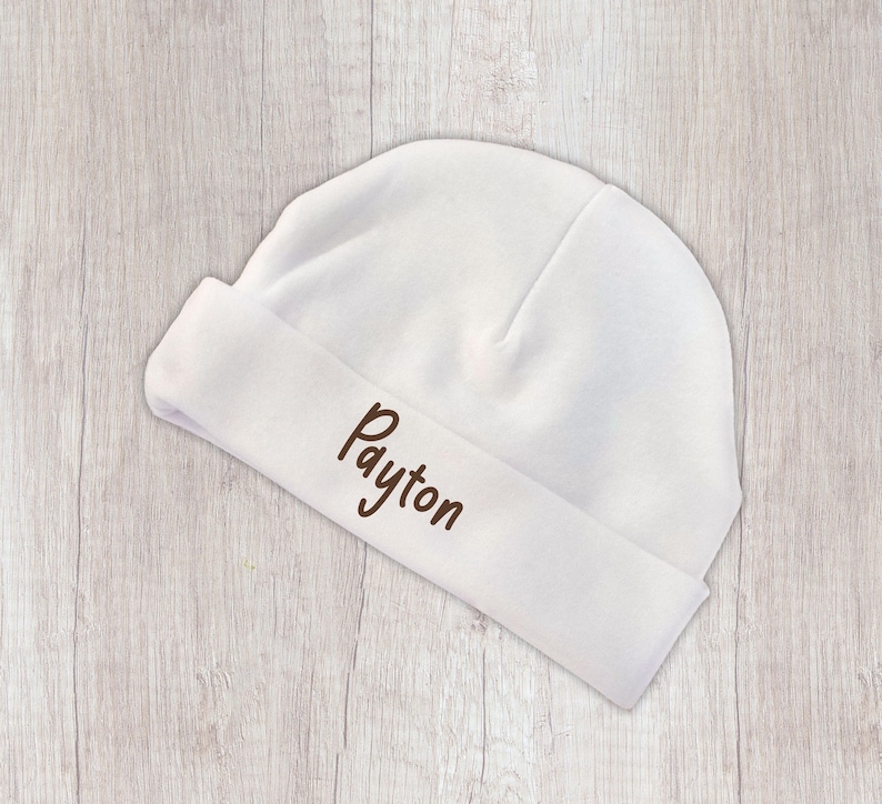 Peut inclure: Un bonnet de b&eacute;b&eacute; blanc avec un revers. Le nom "Payton" est brod&eacute; en marron sur le revers. Le chapeau est fait d'un tissu doux et est con&ccedil;u pour les nouveau-n&eacute;s.