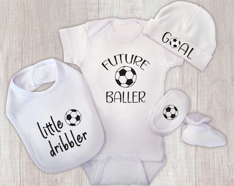 May include: A white baby gift set featuring a bib, onesie, hat, and booties. The bib reads "little dribbler," the onesie says "future baller," and the hat says "goal." Each item has a soccer ball graphic.