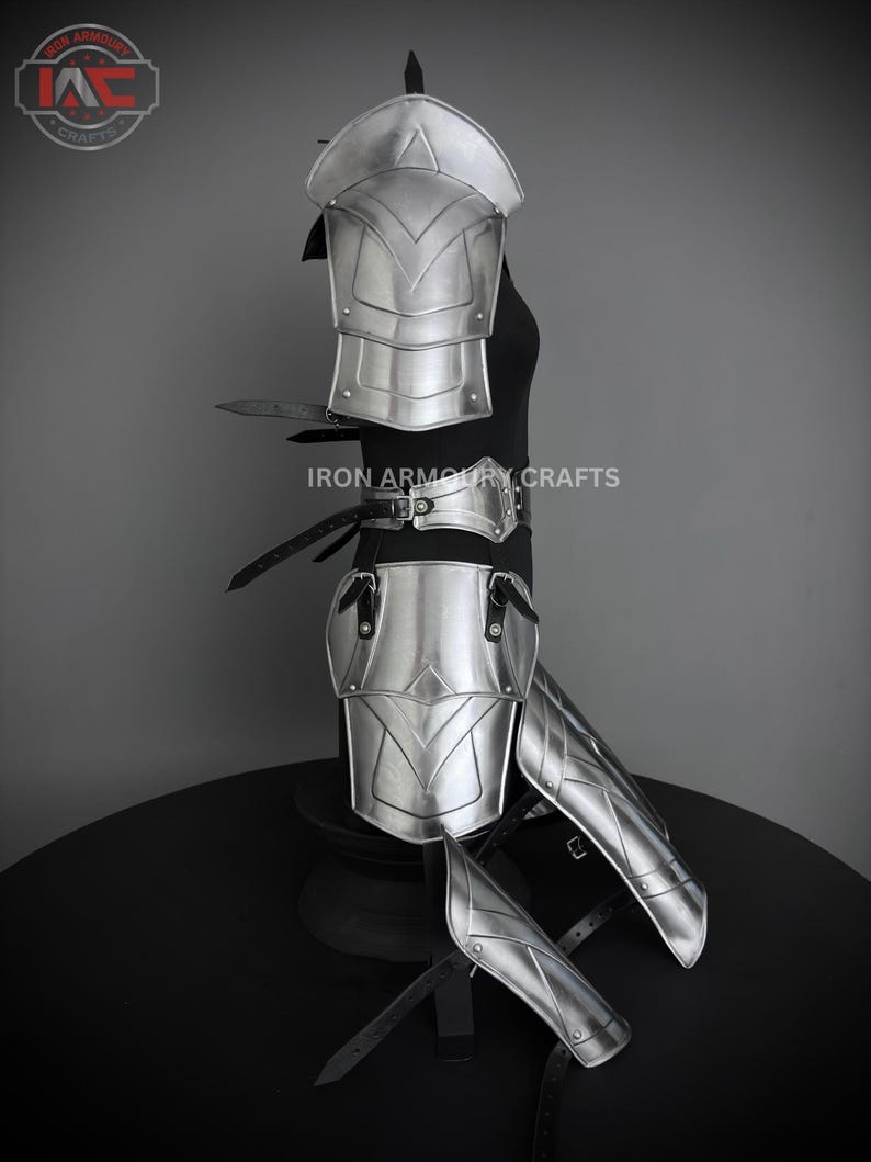 May include: Silver plated armor set for the legs and arms. The set includes a pair of shin guards, a pair of knee pads, a pair of elbow pads, and a pair of shoulder pads. The armor is made of metal and has a polished finish. The armor is displayed on a black stand. "IRON ARMOURY CRAFTS" is printed on the stand.