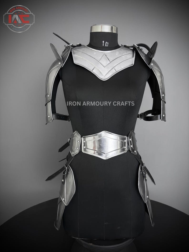 May include: Silver-toned metal armor for the shoulders, chest, and hips. The armor is worn on a black mannequin. The text "IRON ARMOURY CRAFTS" is printed on the mannequin's chest.