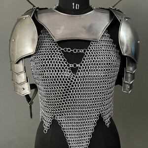 Puede incluir: Armadura de cota de malla plateada con hombreras a juego. La cota de malla tiene forma de V y las hombreras son redondeadas.