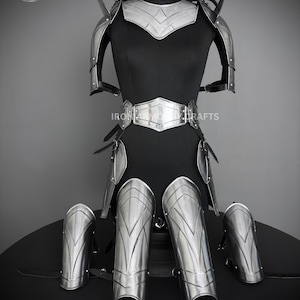 May include: A full suit of silver armor with a decorative design. The armor includes a breastplate, shoulder pads, gauntlets, and leg guards. The armor is displayed on a black mannequin.