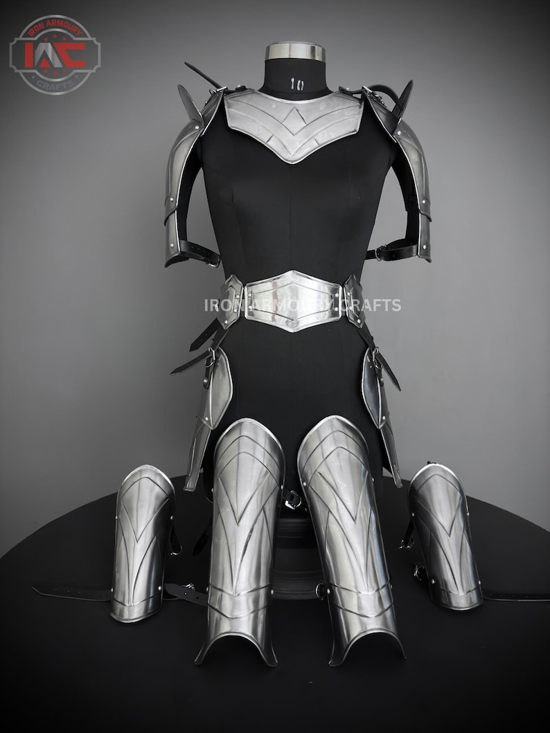 May include: A full suit of silver armor with a decorative design. The armor includes a breastplate, shoulder pads, gauntlets, and leg guards. The armor is displayed on a black mannequin.