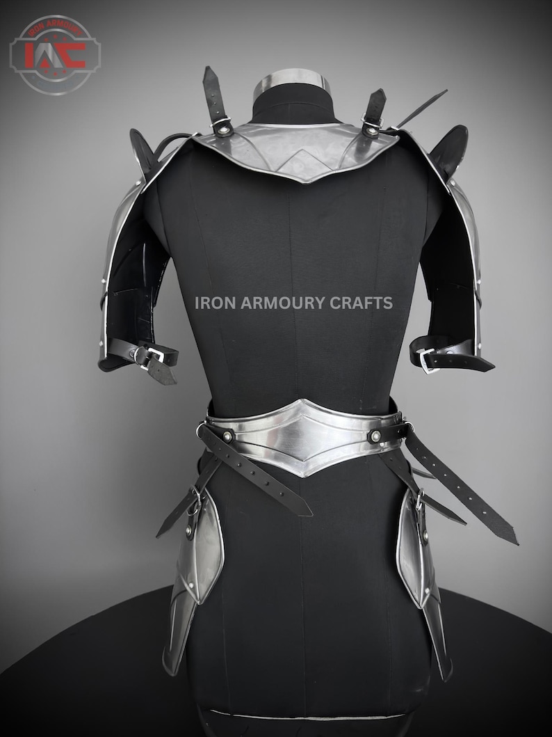 May include: Silver and black armor for the torso, shoulders, and hips. The armor is made of metal plates and leather straps. The armor is displayed on a black mannequin. The text "IRON ARMOURY CRAFTS" is printed on the mannequin.
